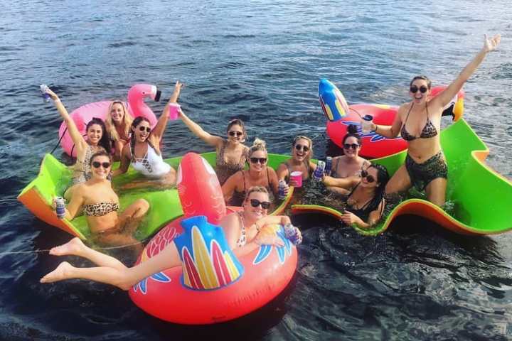 Group of women in swimsuits on large, colorful pool floats in a lake.