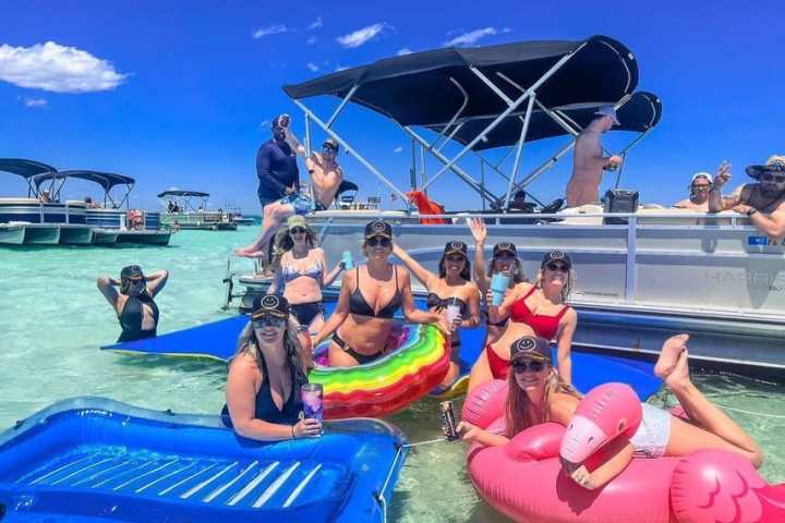 Group of people in swimsuits on a boat and inflatables in clear water under a blue sky.