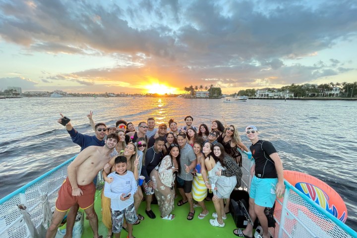 Group of people posing on a boat at sunset over the water.