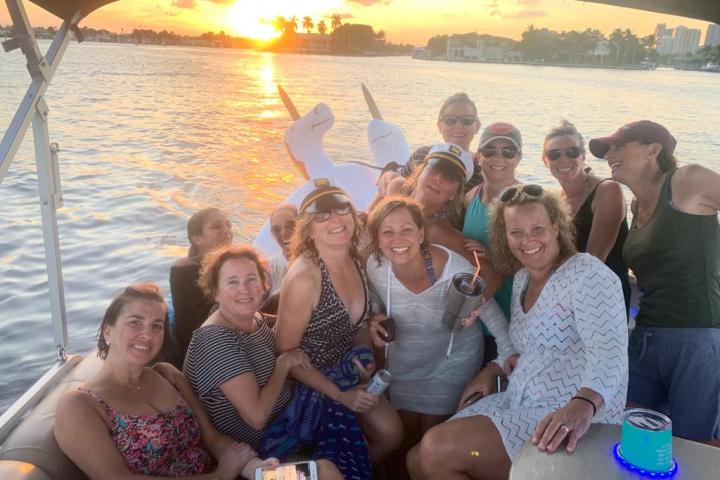 Group of women smiling on a boat at sunset with water and skyline in the background.