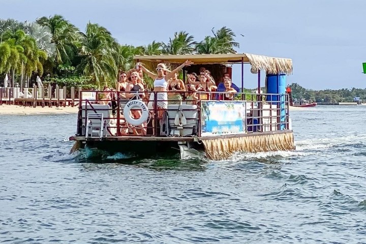 People on a floating bar near a tropical shoreline.